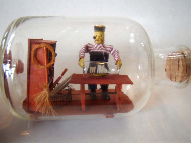 A wonderful small ship-in-a bottle depicting a sailor making a ship-in-a bottle